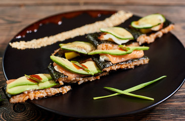 Close up view delicious sushi with nori rice and avocado on black plate served on the wooden table