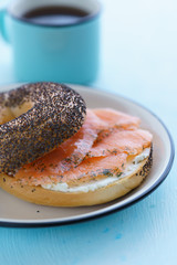 Poppy seeds bagel with cream cheese and smoked salmon served on a white plate with black rim. Blue table, high resolution