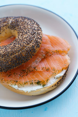 Poppy seeds bagel with cream cheese and smoked salmon served on a white plate with black rim. Blue table, high resolution