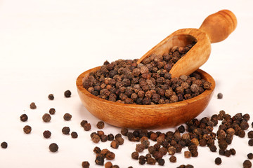 Wooden serving spoon shovel full of black pepper spice balls in wooden bowl isolated over the white background