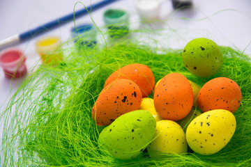 Green nest with colorful Easter eggs decoration, close-up, easter concept, holiday tradition, blurred paints, colorful palette on the background, paint equipment