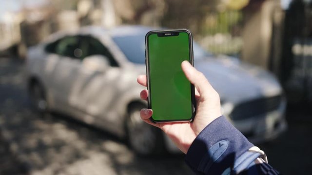 Man hand holding vertically phone in front of a new car. Close-up blur expensive luxury lifestyle chroma key green sreen vertical keeping photo taking picture auto show showroom notification