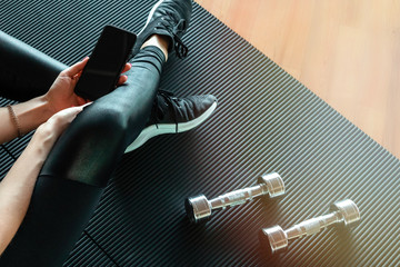 Sporty girl sitting on the floor in the gym with dumbbells and phone. Top view