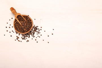 Wooden serving spoon shovel full of black pepper spice balls in wooden bowl isolated over the white background. Copy space