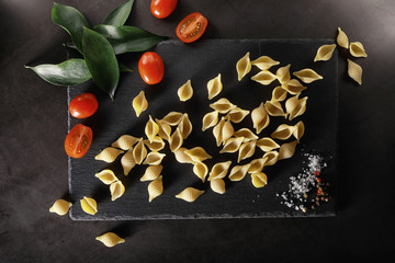 Pasta shells on black stone. Tomatoes and bay leaves with allspice and sea salt.