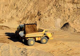 Front-end loader loading with sand a heavy dump truck in a mining quarry