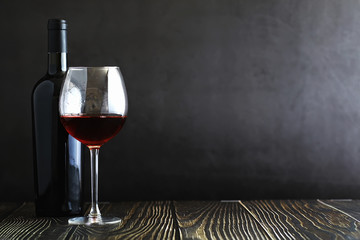 A glass of red dry wine on the table. Dark bottle and glass of wine.