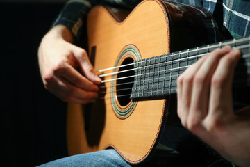 Obraz na płótnie Canvas Man playing on classic guitar against dark background, closeup