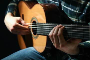 Fototapeta premium Man playing on classic guitar against dark background, closeup