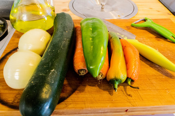 in the photo we can see in a row some vegetables like, zucchini, onion, pepper and carrot. next to the vegetables we have a two-blade peeler with the green handle. You can also see a large sharp knife