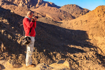 Young man taking a photos of mountain range Red Sea Hills in Arabian desert, Egypt