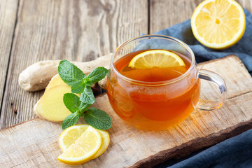 A glass cup of tea with lemon, mint and ginger on wooden rustic table.