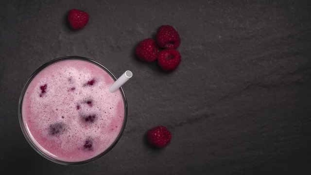 Raspberry milkshake or smoothie with scattered fresh washed organic raspberries on a black stone background with a rack focus zoom effect