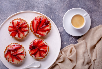 Cupcakes with sliced strawberries and coffee cup on concrete gray background, top view
