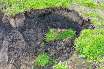 Landslide debris of water-laden masses of soil with the green grass on top in open crack after heavy rain storm. Close up.