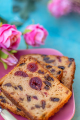 Fruitcake or cupcake on a pink plate. Cookery and dessert. Slices muffins with berry and blurry bouquet of flowers on a blue wooden table. Soft focus. Copy space. Top view. Closeup.