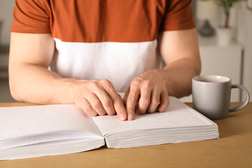 Blind man reading book written in Braille at table, closeup