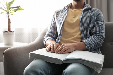 Blind man reading book written in Braille on sofa, closeup