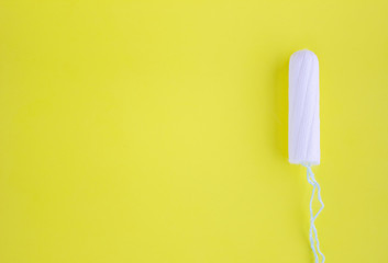One swab with cotton on a yellow background. The concept of the period of the menstrual cycle. Top view, flat lay.