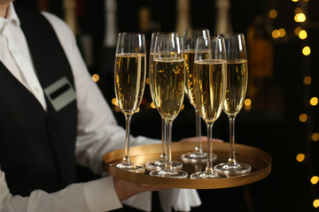 Waiter holding tray with glasses of champagne on blurred background, closeup