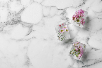 Floral ice cubes on marble background, top view. Space for text