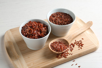 Board with boiled and uncooked brown rice on table