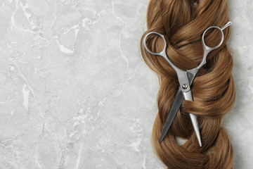 Flat lay composition with brown hair, scissors and space for text on grey background. Hairdresser...