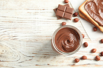 Flat lay composition with glass jar of tasty chocolate cream and hazelnuts on wooden background. Space for text