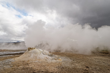Volcanic landscape with a large fumarole, which releases a lot of steam, in the background further steam escape, wind lets the steam in the horizontal direction deduct, contrasting sky - Iceland