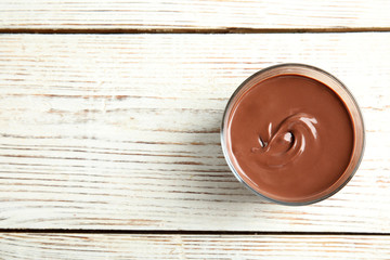 Glass with tasty chocolate cream on wooden background, top view. Space for text