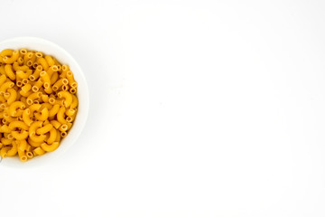 Uncooked macaroni in a bowl isolated on white background with space for text, flat lay concept. 