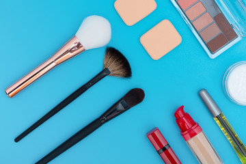 Decorative cosmetics, makeup products and brushes on blue background