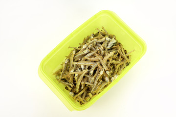 Dried anchovies in a green plastic container on isolated white background
