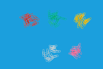 five heaps of different in colours paper clips lying on a blue background. free space for advertising text. top view. concept of office chancery