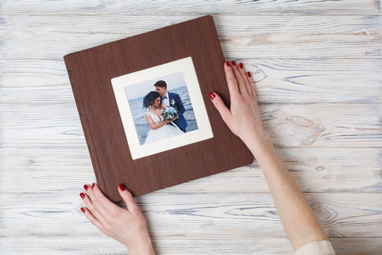 brown photo book with  leather cover.  stylish wedding photo album. a person opens a photobook. Family photoalbum on the table. the womans hand holding a family photo album