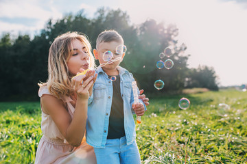 Mother and little son blowing soap bubbles outdoor