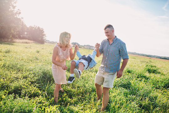Mother and father swinging son in sunnny summer day