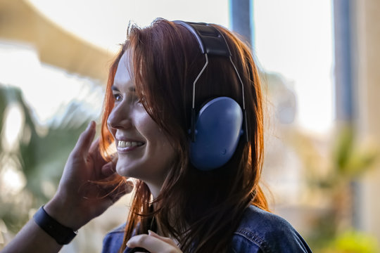 Beautiful red-haired woman puts on antinoise headphones, preparing to fly a helicopter