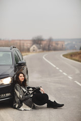 Naklejka premium The girl is sitting on the road near a black car