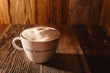 Cup of coffee with soy milk foam on wooden table in moody morning light - angled