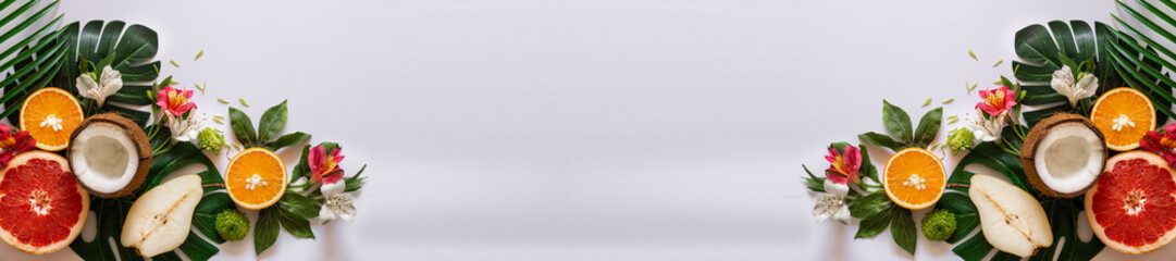 Summer tropical theme background or template with a space for a text, various fruits, green leaves and flowers. Bright summer background