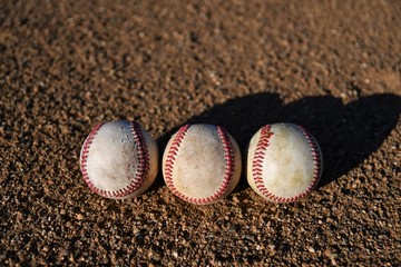 Overhead photo of three game used baseballs on a baseball infield on a sunny day