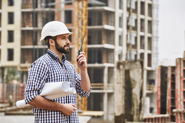 Working process. Professional young at construction builder in white protective helmet talking to...