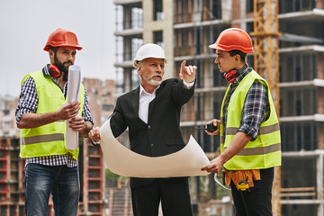 Plan of building. Main engineer in formal wear and white helmet holding a sketch of new project and...