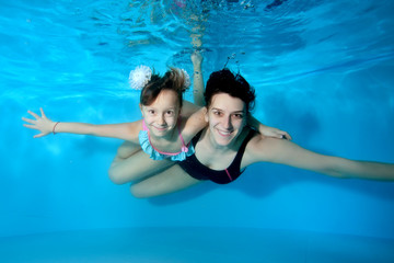 Obraz na płótnie Canvas Underwater portrait of a little girl and her mother in the pool. They swim and cuddle underwater with their eyes open. Close up. Horizontal view