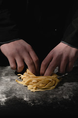 Chef hands making spaghetti, pasta, noodles with fresh pasta on black table with.