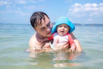 Happy laughing infant baby with dad having fun in the sea. Father teaches daughter to swim and water.