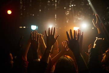 Fototapeta na wymiar Crowd of unrecognizable people standing in dark club and waving hands in air while waiting for performer on stage