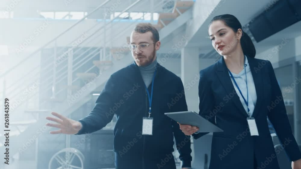 Poster female and male engineer enter a high tech development facility holding a tablet computer. they walk