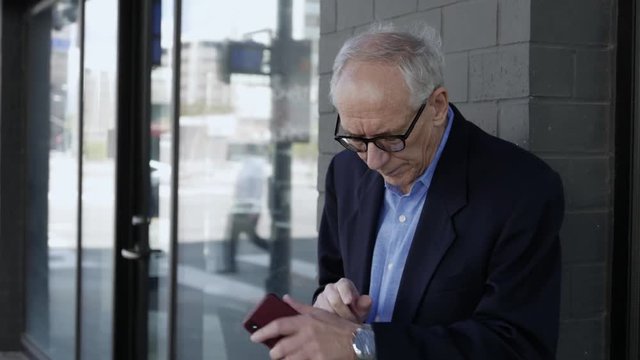 Elderly man uses his smartphone downtown.